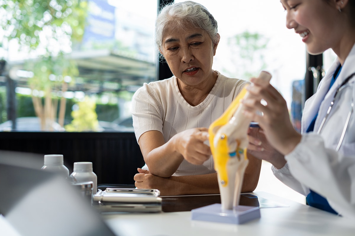 Doctor holding a model of the knee joint while talking with a patient Doctor holding a model of the knee joint while talking with a patient